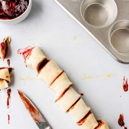 A roll of dough with raspberry jam and a knife next to it.