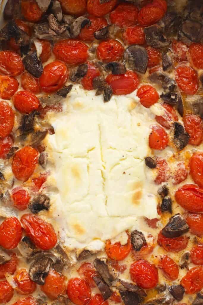 Baked cream cheese surrounded by tomatoes and mushrooms after being baked.