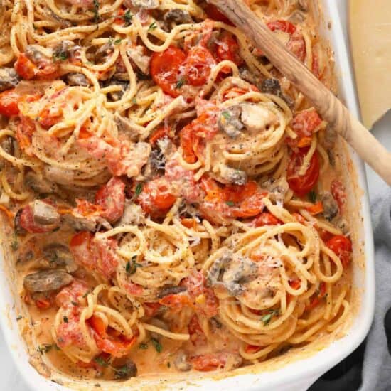 spaghetti with mushrooms and tomatoes in a white baking dish.