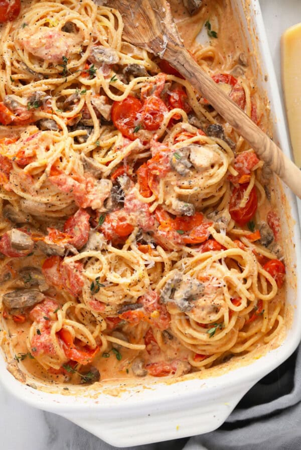 spaghetti with mushrooms and tomatoes in a white baking dish.