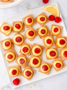 a plate with lemon and raspberry tarts on it.