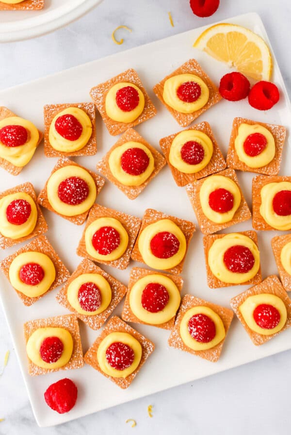 a plate with lemon and raspberry tarts on it.