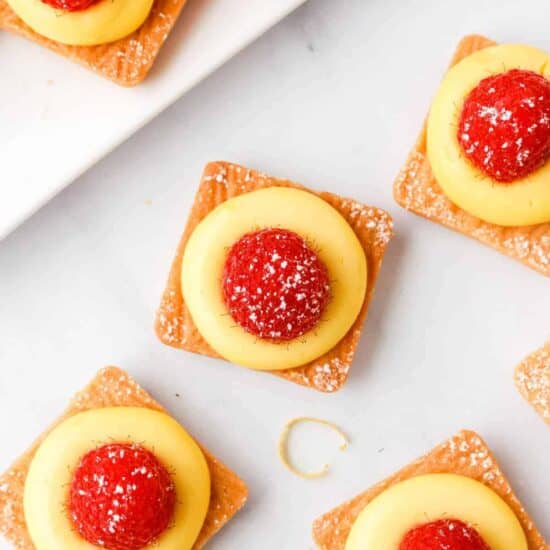 a white plate with lemon tarts and raspberries on it.