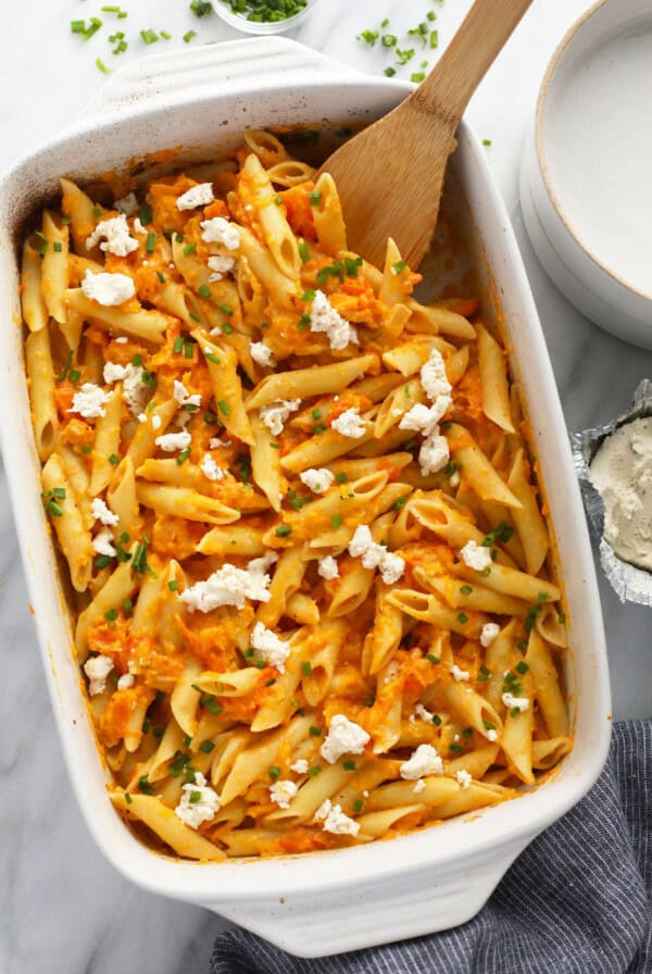 penne pasta with carrots and feta in a white dish with a wooden spoon.