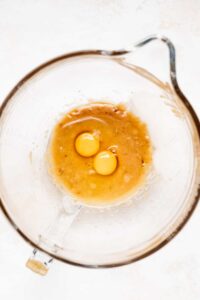 two eggs in a glass bowl on a white surface.