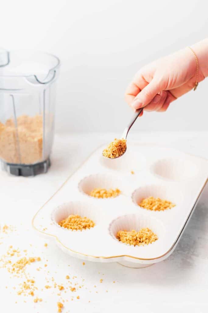 Graham cracker crust being spooned into muffin liners.