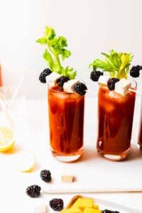 Three glasses of bloody mary served with blackberry and cheese skewers.