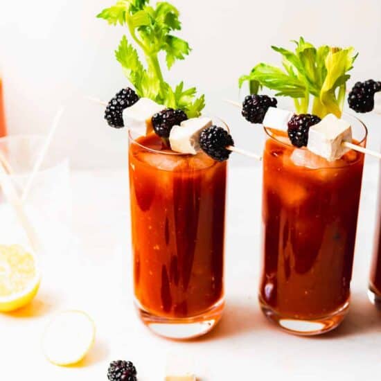 Three glasses of bloody mary served with blackberry and cheese skewers.