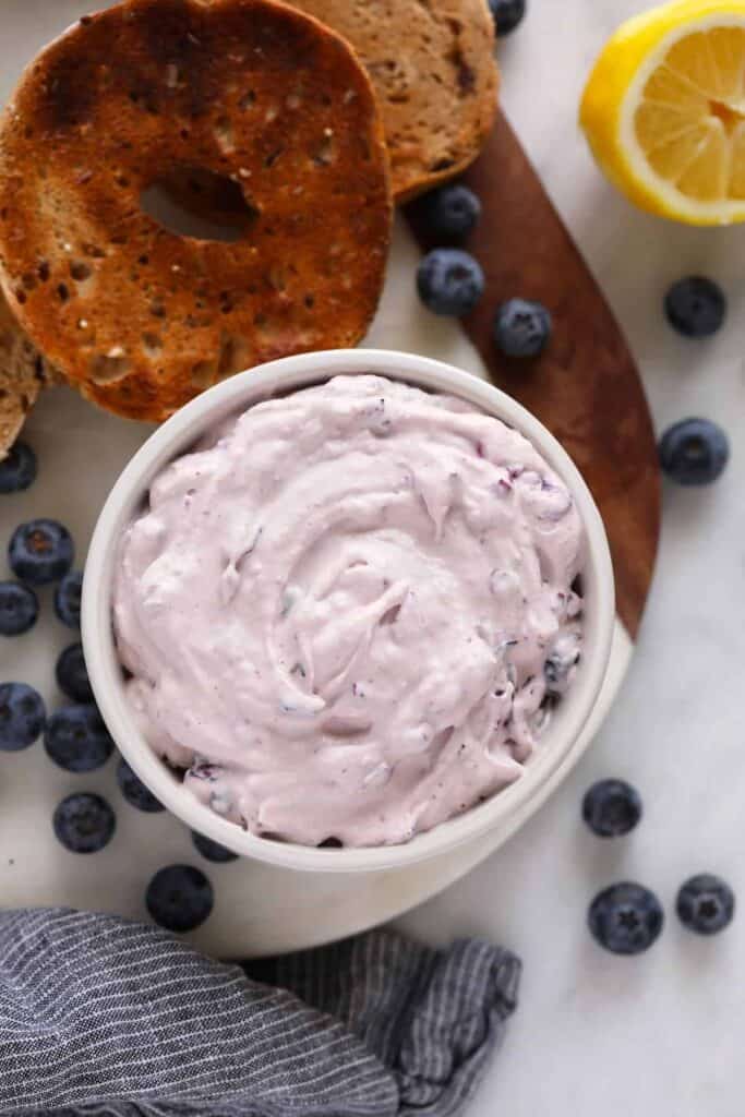 A bowl of blueberry cream cheese on a cutting board. 