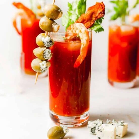 a glass of bloody mary with a blue cheese stuffed olive skewer