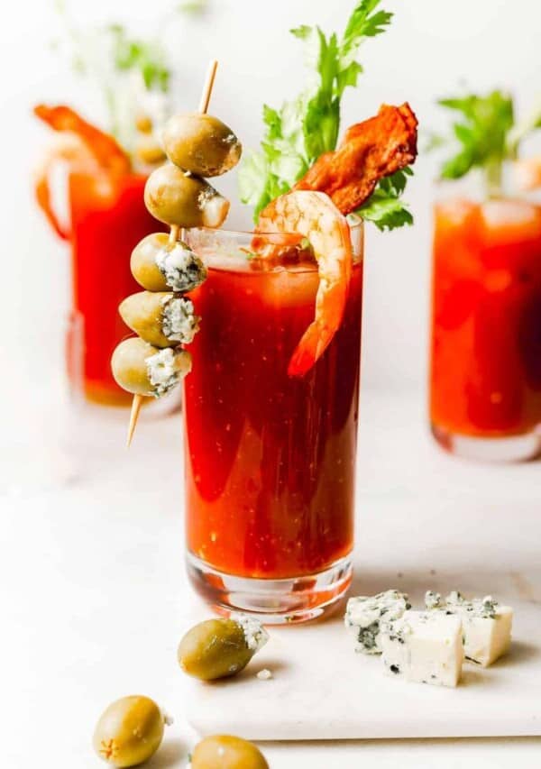 a glass of bloody mary with a blue cheese stuffed olive skewer