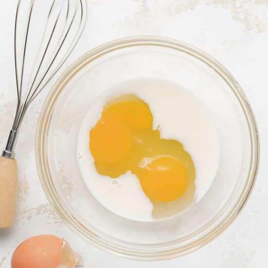 eggs in a bowl next to a whisk.