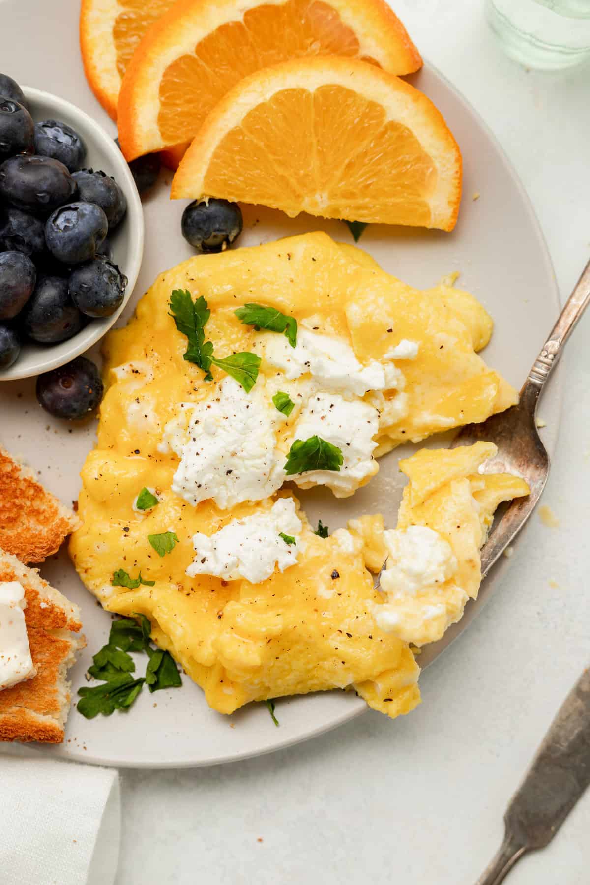 Goat cheese scrambled eggs on a plate with blueberries and orange slices. 