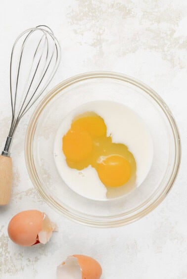 eggs in a bowl next to a whisk.