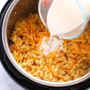 a person pouring milk into a pot of macaroni and cheese.