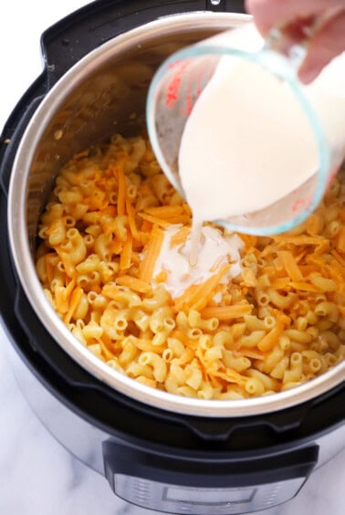 a person pouring milk into a pot of macaroni and cheese.