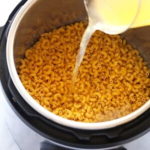 a person pouring orange juice into a pot of macaroni and cheese.