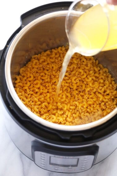 a person pouring orange juice into a pot of macaroni and cheese.
