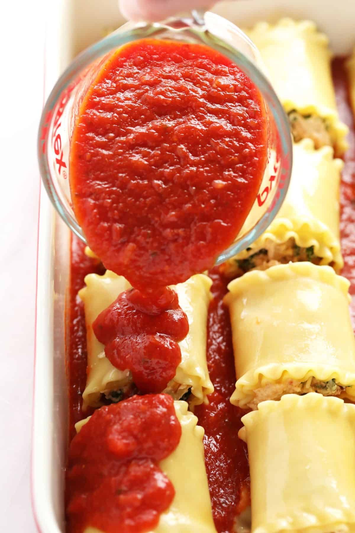 Pouring marinara sauce over lasagna roll ups. 