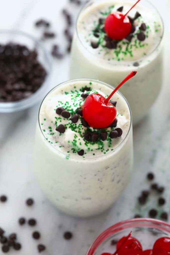 Shamrock shake in a glass with whipped cream, a cherry on top, and green sprinkles. 