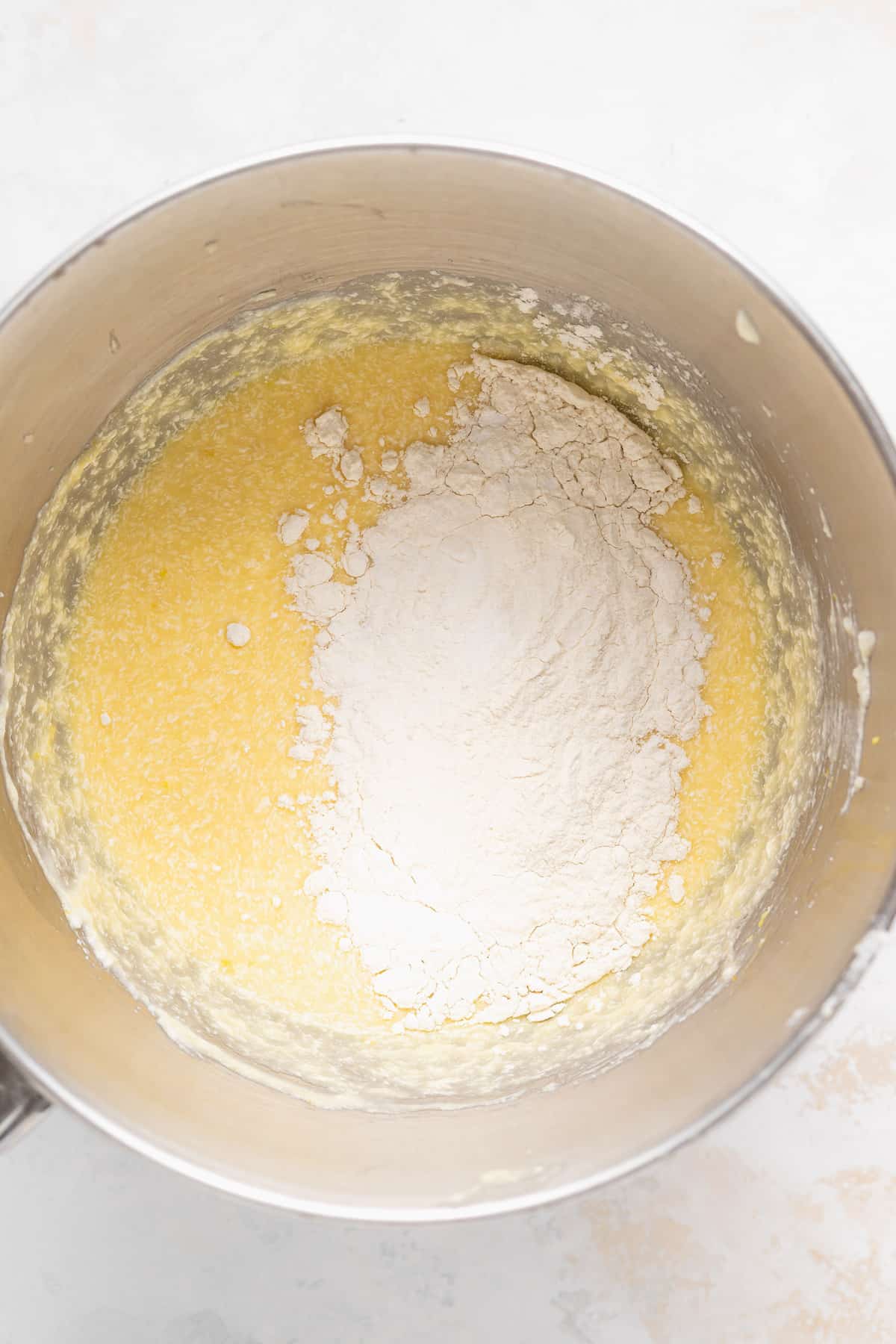 dry ingredients being added to lemon ricotta cake batter in a bowl