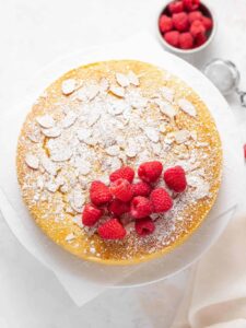 a cake with raspberries and powdered sugar on a white plate.