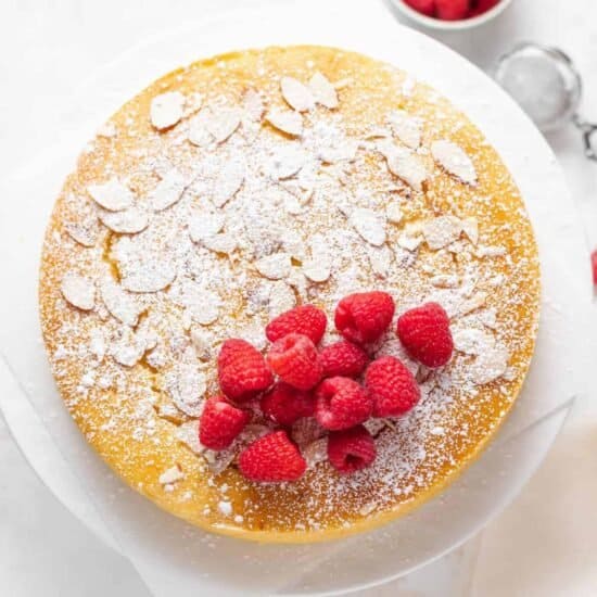 a cake with raspberries and powdered sugar on a white plate.