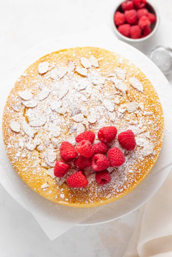 a cake with raspberries and powdered sugar on a white plate.
