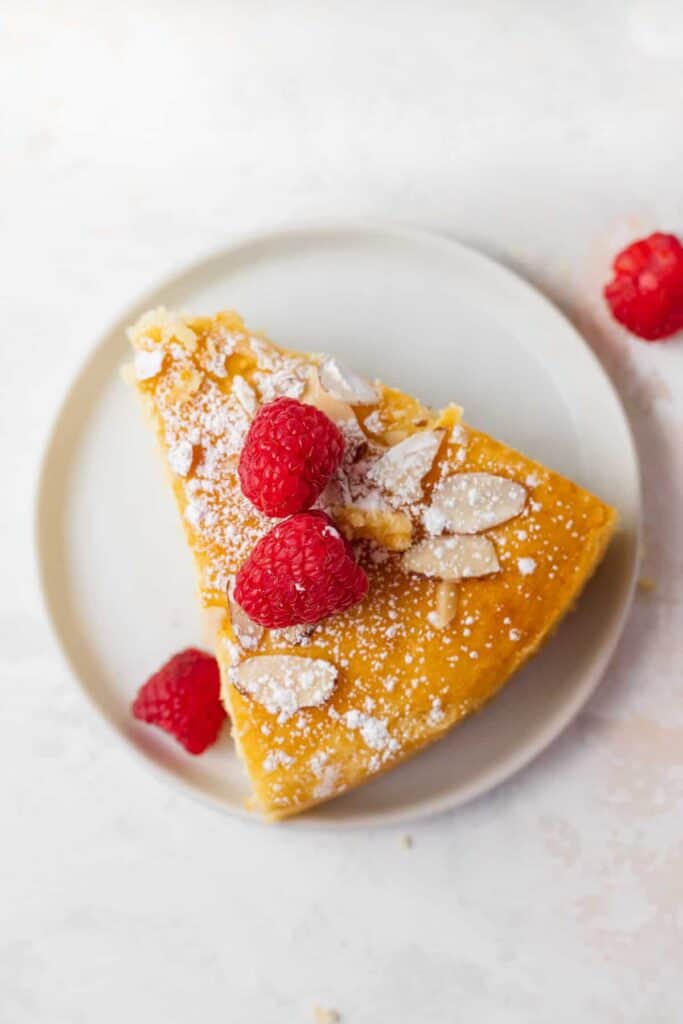 slice of lemon ricotta cake on a plate with fresh raspberries on the top