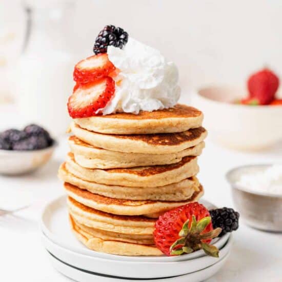 a stack of pancakes with whipped cream and berries.
