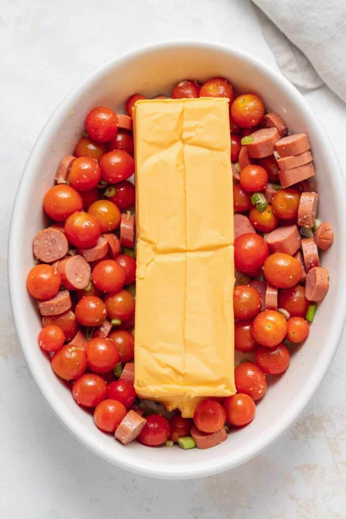 Baked velveeta pasta ingredients in a casserole dish with velveeta in the middle of the casserole dish. 