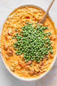macaroni and peas in a white bowl with a wooden spoon.