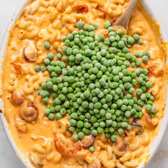 macaroni and peas in a white bowl with a wooden spoon.