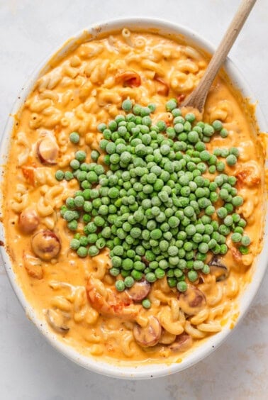 macaroni and peas in a white bowl with a wooden spoon.