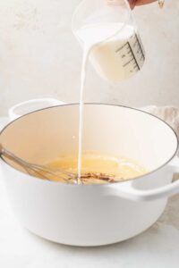 A person making white cheddar mac and cheese by pouring milk into a pan.