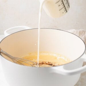 A person making white cheddar mac and cheese by pouring milk into a pan.