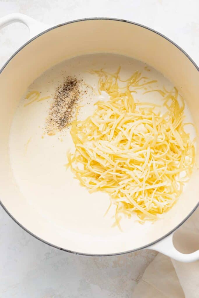 adding white cheddar cheese to roux in pot