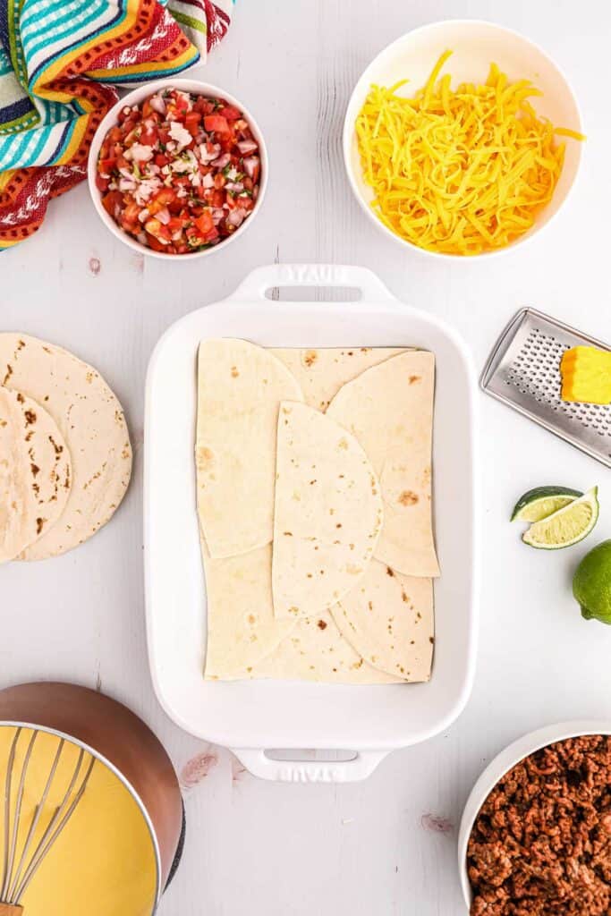 A casserole dish with tortillas laid out on the bottom. 