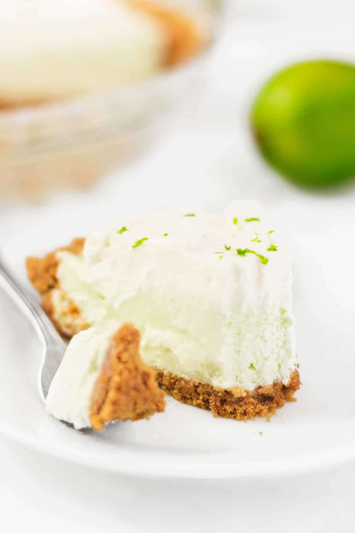 A fork taking a bite out of one pieces of key lime pie. 