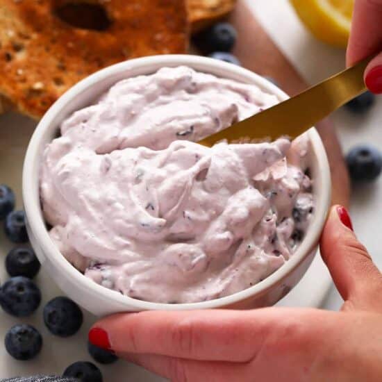 a person is dipping a spoon into a bowl of blueberry dip.