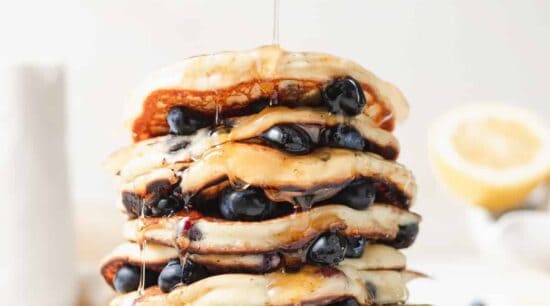 a stack of blueberry pancakes being drizzled with syrup.