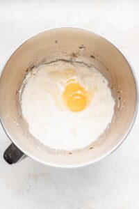 An egg cracked in a mixing bowl, ready for chocolate chip ricotta muffins.