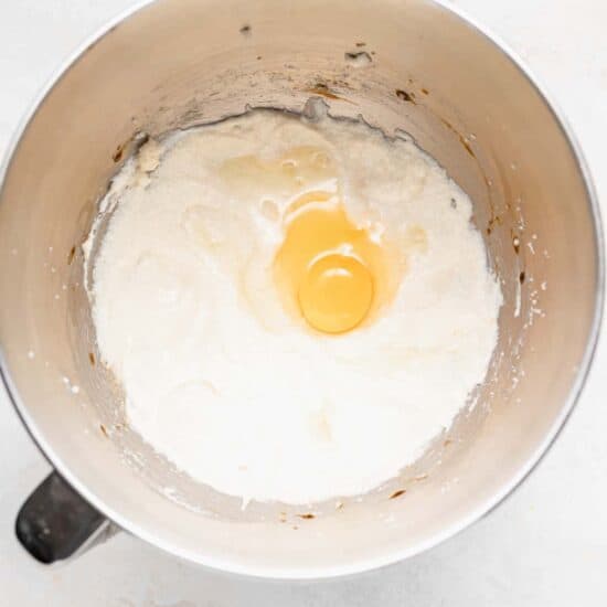 An egg cracked in a mixing bowl, ready for chocolate chip ricotta muffins.