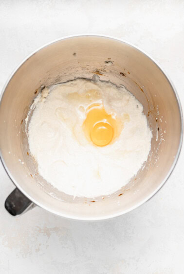 An egg cracked in a mixing bowl, ready for chocolate chip ricotta muffins.