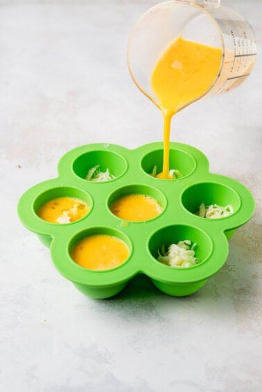Instant pot cheesy egg bites being poured into a green muffin tin.