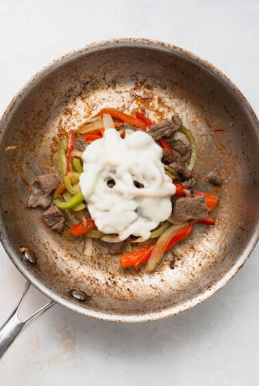 a frying pan with meat, peppers and sour cream.