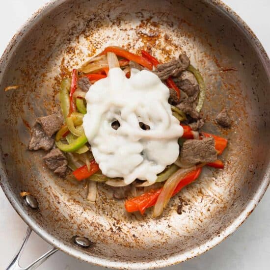 a frying pan with meat, peppers and sour cream.