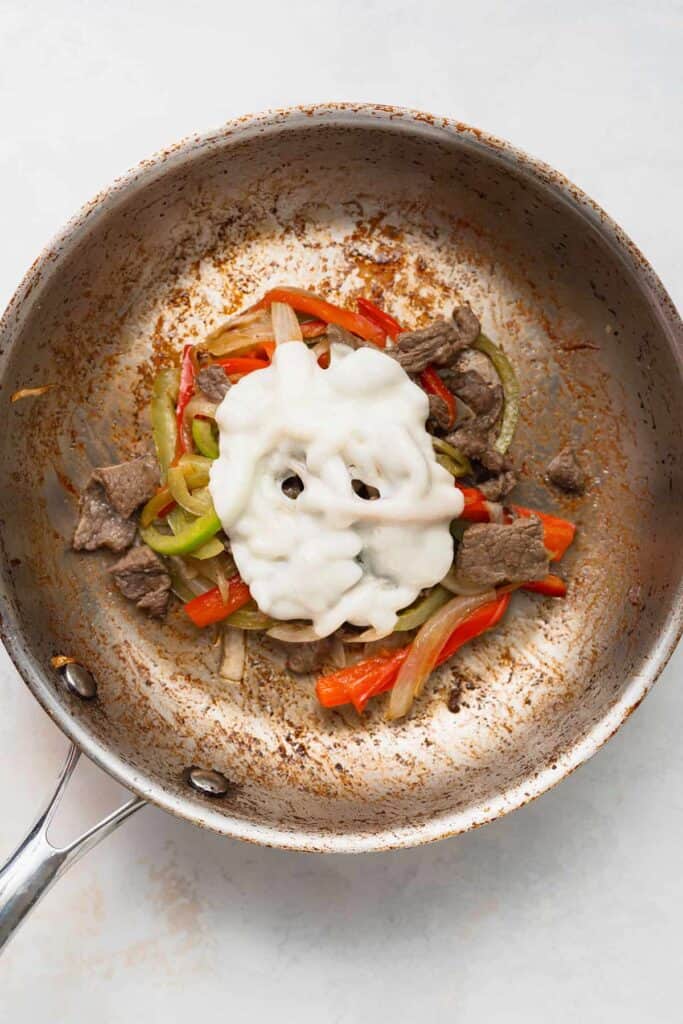 Melting cheese over peppers and onions in a saute pan. 