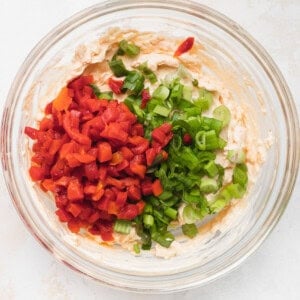 a bowl filled with red peppers and green onions.