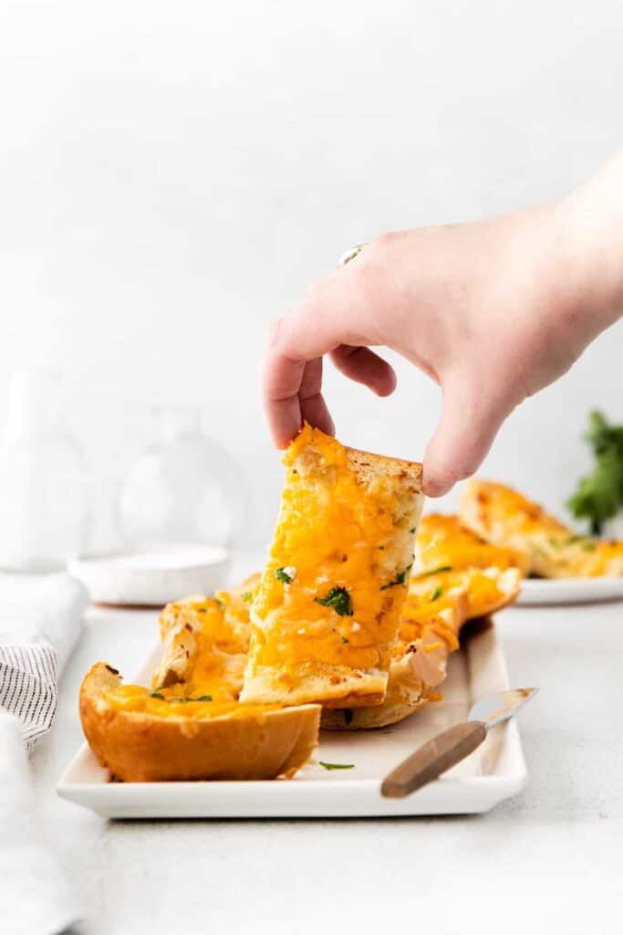 A hand picking up a piece of cheesy garlic bread. 